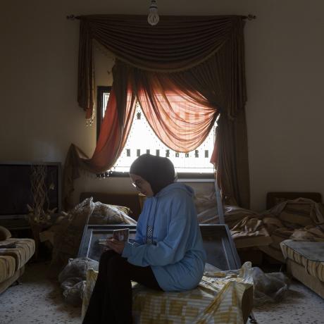 A young woman from Lebanon looks at a family photo album in her living room, which was damaged after it was bombed by Israeli forces. 